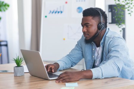 Interprète Trad Lingo 3 Customer support concept. Young african american manager with headset using laptop at workplace, checking client's data to solve issues.